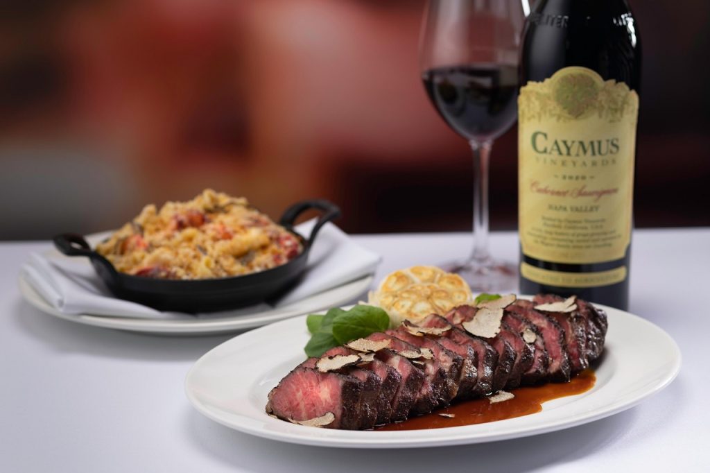 Steak dish with truffle slices, wine bottle, and side of macaroni from the Capital Grille menu.