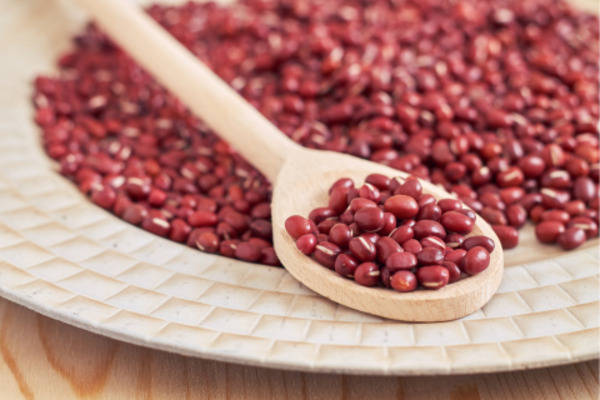 Wooden spoon filled with red beans resting on a plate of scattered red beans, highlighting their rich color and small size.