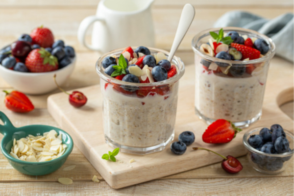 Two oatmeal jars topped with fresh berries, almonds, and mint on a wooden board.