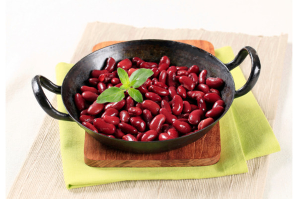 Cooked kidney beans served in a black dish, garnished with a fresh basil leaf, showcasing their rich red color and smooth texture.